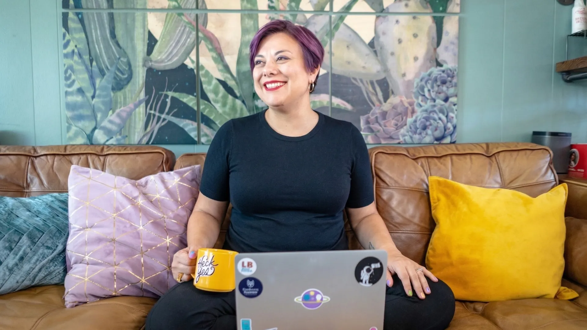 Hazel Quimpo sitting on a leather couch with a laptop and yellow mug, smiling — AI teacher and marketing strategist based in Milwaukee, Wisconsin